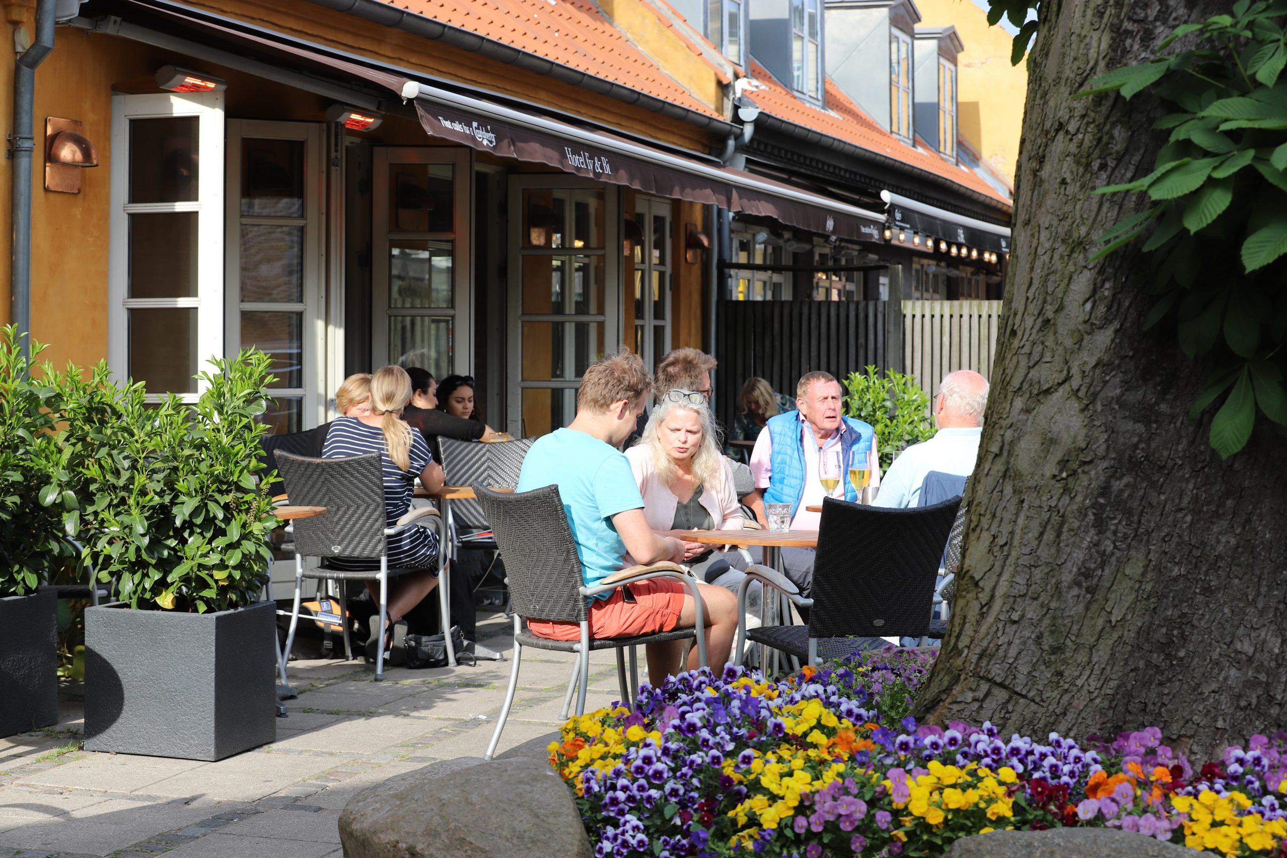 Gæster nyder solen ved caféens borde foran den gule bygning på Valby Langgade